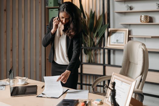 A Woman in Black Blazer Talking on the Phone while Looking at the Documents on the Table